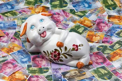 Mit wenig Geld trotzdem Investieren - so geht's Ein Sparschwein liegt auf Schweizer Banknoten.