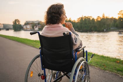 Finanzielle Gefahren bei langer Krankheit - und wie sie sich eindämmen lassen Eine ältere Frau sitzt im Rollstuhl und blickt auf den Fluss.