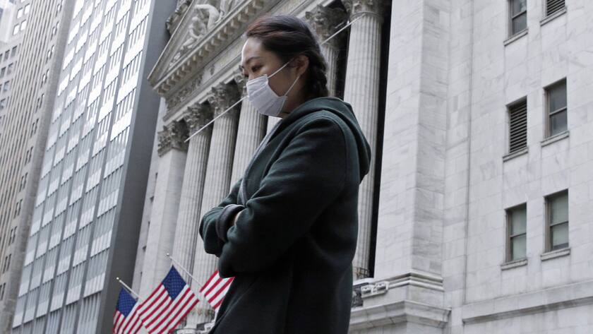 Eine Frau mit Schutzmaske in New York, im Hintergrund der Sitz der New York Stock Exchange an der Wall Street.