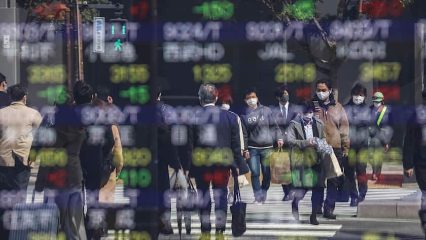 Das Spiegelbild einer Kurstafel in Tokio mit Passanten, die eine Kreuzung überqueren.