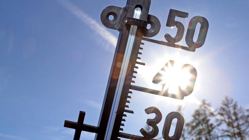 Symbolbild, ein Thermometer vor blauem Himmel und der Sonne.