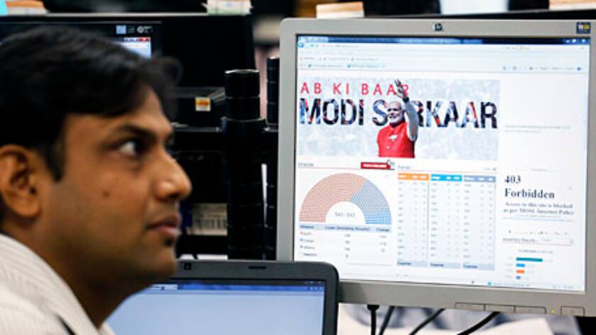A trader sits next to a screen showing a graphic of Narendra Modi, prime ministerial candidate of the Bharatiya Janata Party (BJP), on the trading floor of the Motilal Oswal Financial Services Ltd. office in Mumbai, India, on Friday, May 16, 2014.