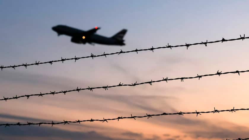 Zölle als Handelsschranken - sinnbildlich: ein Flugzeug startet am Flughafen Köln Bonn gesehen durch Stacheldraht ausserhalb des Rollfelds.