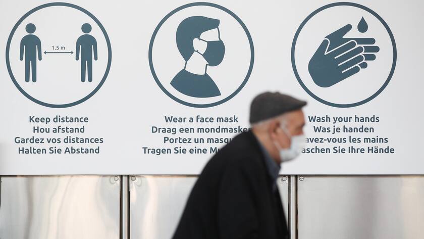 Reisender mit Gesichtsmaske am Flughafen Zaventem in Brüssel - im Hintergrund wird auf die Regeln hingewiesen.
