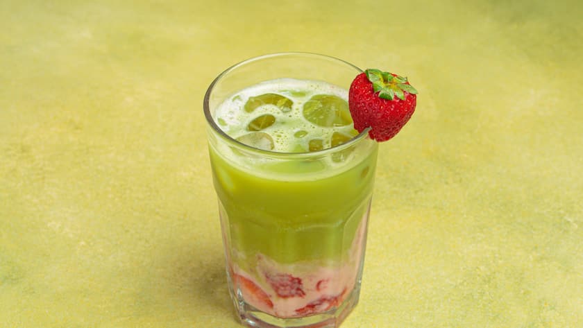 Geeister Matcha Latte mit Erdbeerpüree und Eiswürfeln.