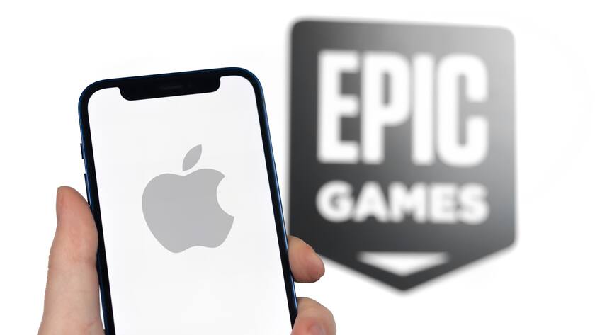 Das Apple-Logo auf einem Smartphone mit dem Logo von Epic Games im Hintergrund.