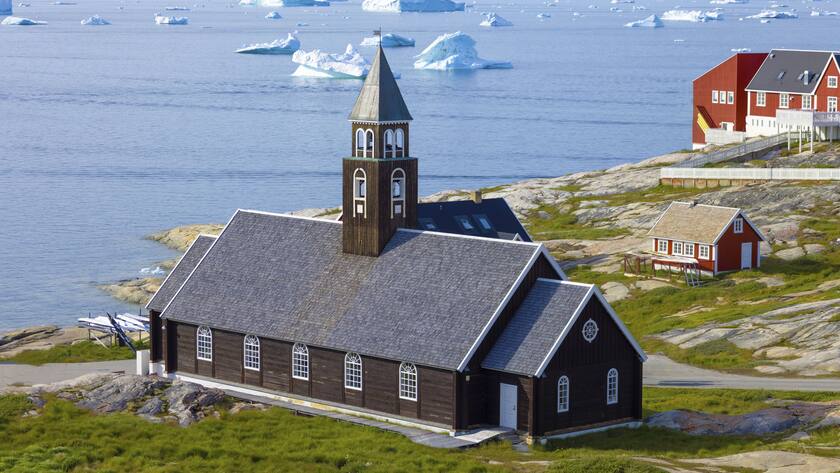 Eine klassische Kirche in Grönland vor einem Fjord mit Eisschollen.