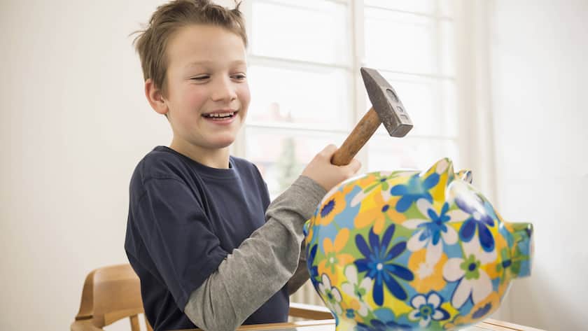 Ein Bub hält spasseshalber einen Hammer über sein Sparschwein (2014).