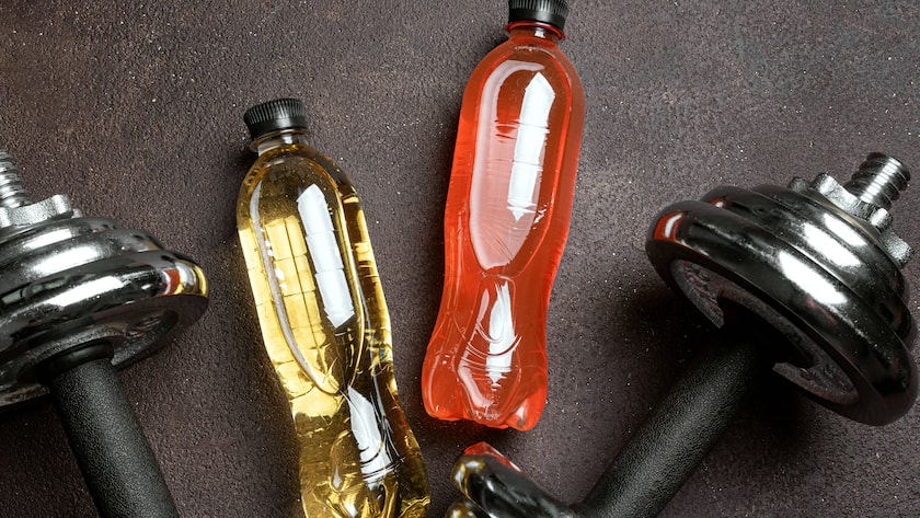 Isotonisches Sportgetränk mit Hanteln auf dunklem Hintergrund.