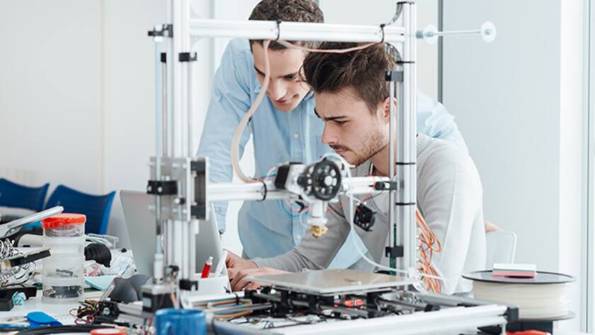 Zwei junge Ingenieure am Laptop hinter einem 3D-Drucker
