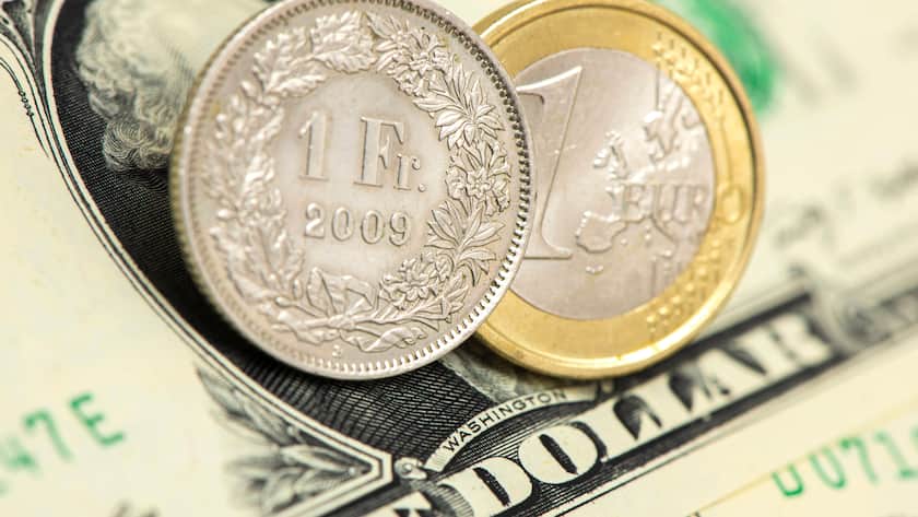 Auf einem US-Dollar-Schein liege eine Münze Schweizer Franken und eine Euromünze.