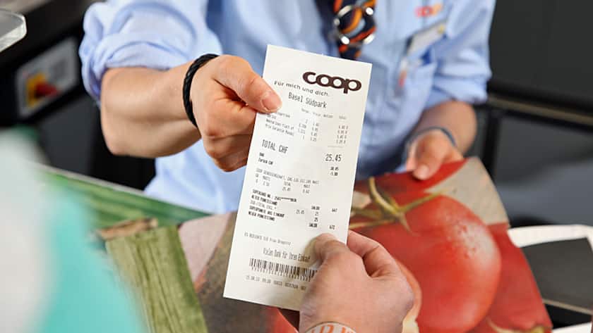 Eine Coop-Verkäuferin reicht der Kunden den Kassenzettel.