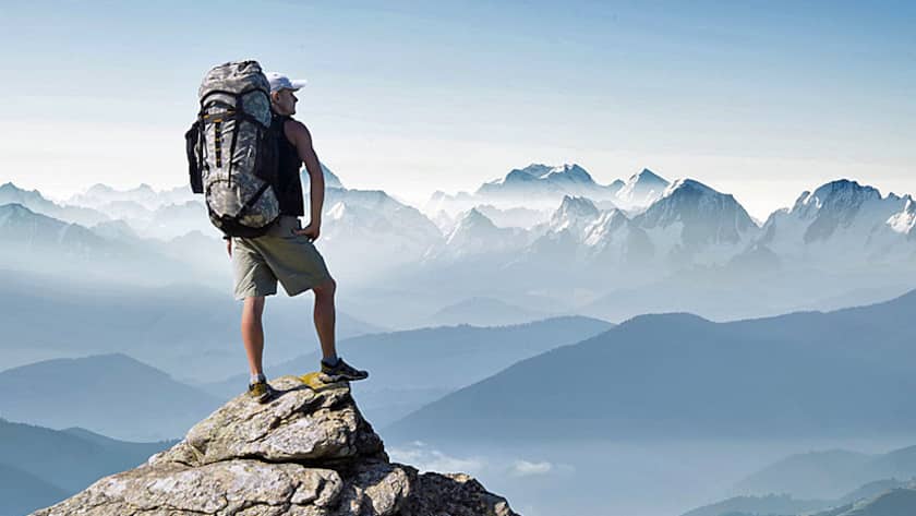 Ein Bergsteiger steht auf dem Gipfel und geniesst die Aussicht.