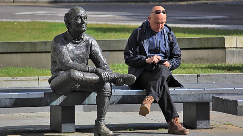 Ein Mann checkt bei einer Pause auf einer Parkbank sein Smartphone.