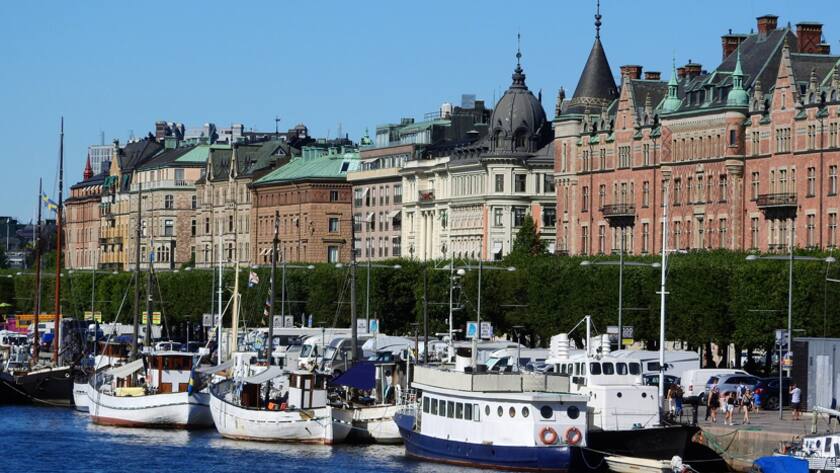 Uferpromenade in Stockholm mit historischen Bauten und zahlreichen Schiffen.