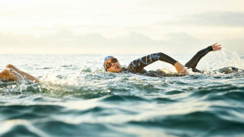 Determined mature woman with friends swimming in sea. Females are doing water sports against sky during sunset. They are representing healthy lifestyle.
