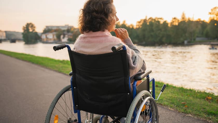 Eine ältere Frau sitzt im Rollstuhl und blickt auf den Fluss.