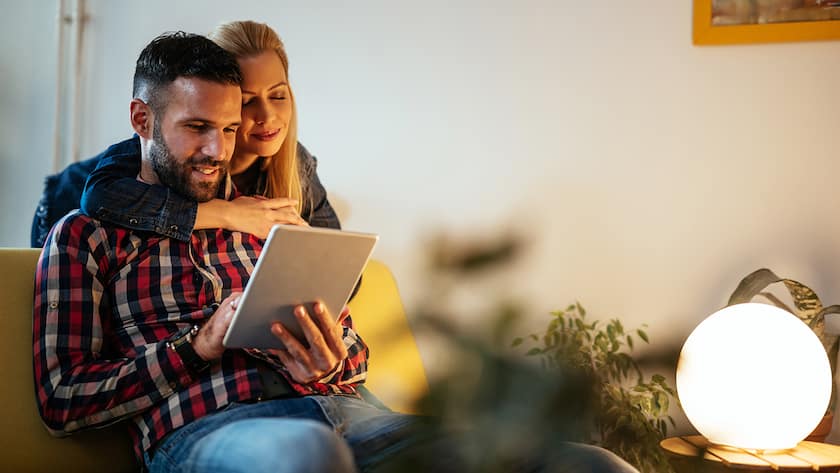 5 Gründe, warum du diesen Herbst und Winter ein VPN brauchst Close up portrait of an attractive married couple using digital tablet. Wife is hugging her husband from behind. They are both feeling happy and in love.