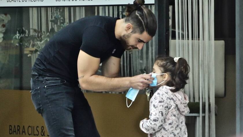 Ein Mann setzt in Genf einem Kind eine Maske auf - Die Diskussion um Schutzmasken nimmt in der Schweiz Fahrt auf. Kinder gelten allerdings inzwischen als kaum ansteckend.