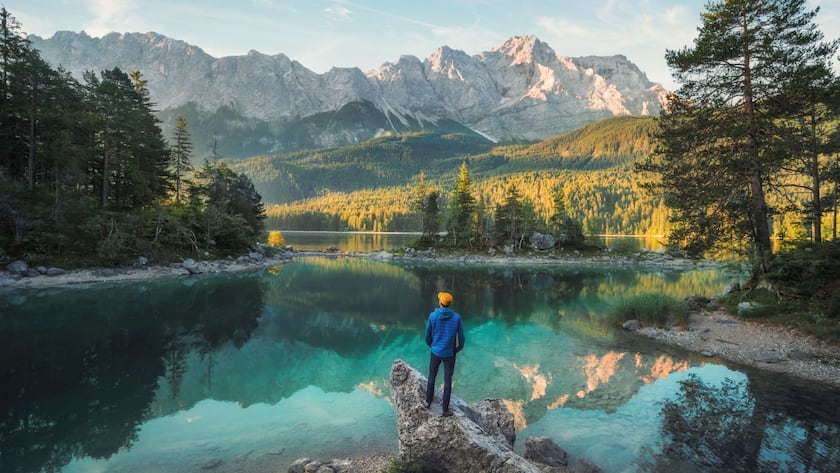 Man enjoying the amazing morning scenery at a gorgeous lake in the Bavarian Alps, with teal water reflecting the view of the mountain range and the nice clouds