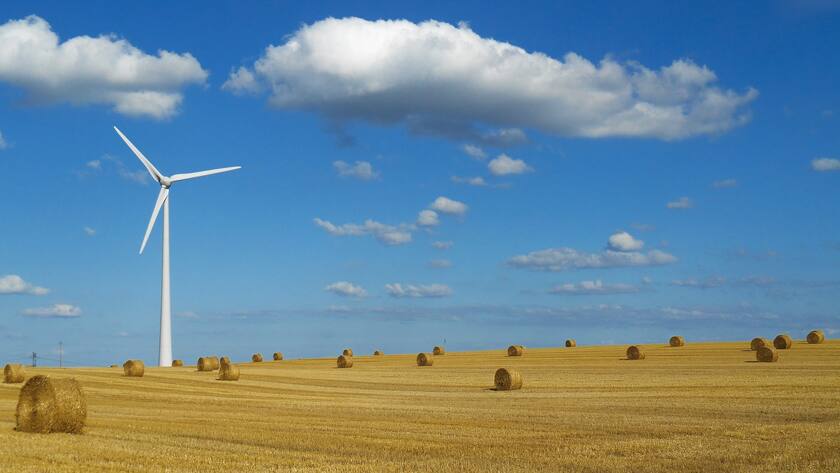 Erzeugung von Windenergie, im leichtenden Strohfeld, unter blauem Himmel.